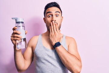 Young handsome sportsman with beard wearing sleeveless t-shirt drinking bottle of water covering...