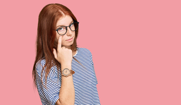 Young read head woman wearing casual clothes and glasses pointing to the eye watching you gesture, suspicious expression