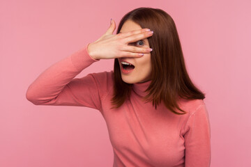 Nosy brunette woman in pink sweater spying through hole in fingers pretending to close eyes with...