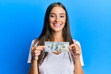 Young hispanic woman holding 100 dollar banknote smiling with a happy and cool smile on face. showing teeth.