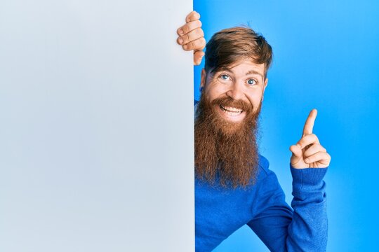 Young irish redhead man holding blank empty banner smiling happy pointing with hand and finger to the side