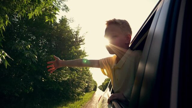 Happy child stretched out his hand from the car window. Happy family. Child hand plays with the wind. Free kid waving from the car window. Kid drives a car and waves his hand. Happy family concept