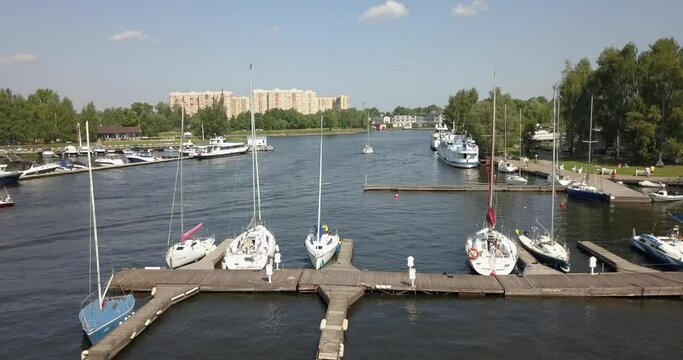 4K high quality calm windless bright summer morning aerial video of Moscow Channel yacht club embankment, green trees, wooden pier and shore with moored anchored boats and yachts near Moscow, Russia