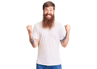 Fototapeta premium Handsome young red head man with long beard wearing casual white tshirt celebrating surprised and amazed for success with arms raised and open eyes. winner concept.