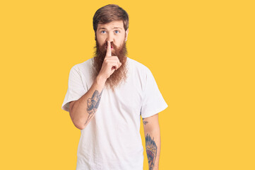 Handsome young red head man with long beard wearing casual white tshirt asking to be quiet with finger on lips. silence and secret concept.