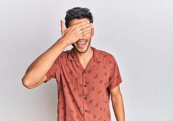 Young handsome man wearing casual summer clothes smiling and laughing with hand on face covering eyes for surprise. blind concept.