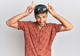Young handsome man wearing casual summer clothes posing funny and crazy with fingers on head as bunny ears, smiling cheerful