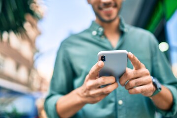 Young latin man smiling happy using smartphone walking at the city.