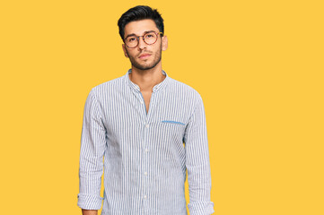 Young handsome man wearing casual clothes and glasses relaxed with serious expression on face....
