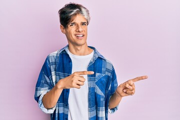 Young hispanic man pointing with fingers to the side clueless and confused expression. doubt...