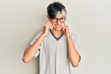 Young hispanic man wearing casual clothes and glasses covering ears with fingers with annoyed expression for the noise of loud music. deaf concept.