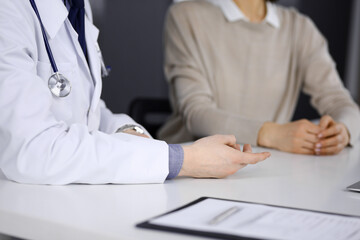 Unknown male doctor and patient woman discussing something while sitting in clinic. Best medical service in hospital, medicine, pandemic stop