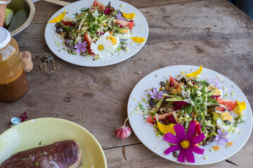 salade composée avec des fleurs colorées sur une table en bois où l'on prépare un repas avec de la viande