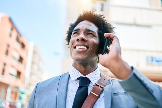 Young african american businessman wearing suit smiling happy. Standing with smile on face having conversation talking on the smartphone at town street.