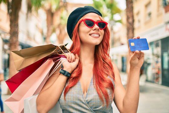 Young redhead girl wearing french style holding shopping bags  and showing credit card at the city