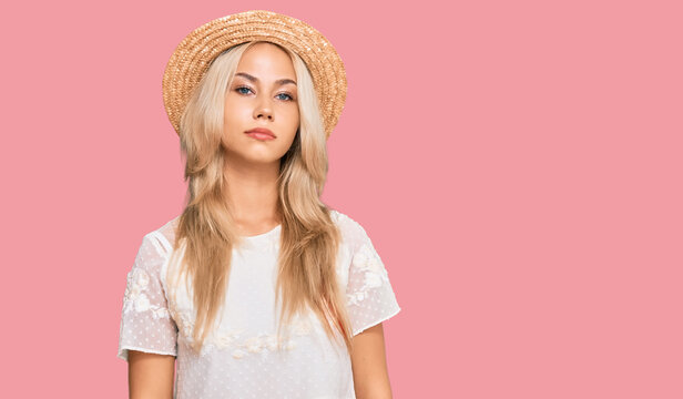 Young blonde girl wearing summer hat relaxed with serious expression on face. simple and natural looking at the camera.