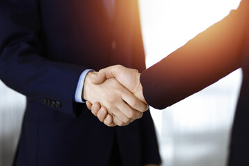 Business people shaking hands, close-up. Group of unknown businessmen standing in a sunny modern office. Teamwork, partnership and handshake concept