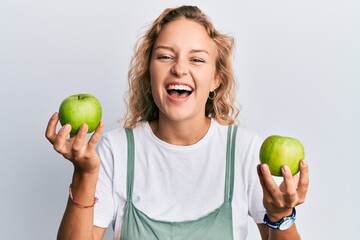Beautiful caucasian woman holding green apples smiling and laughing hard out loud because funny crazy joke.