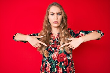 Young caucasian woman with blond hair pointing with fingers to herself skeptic and nervous,...