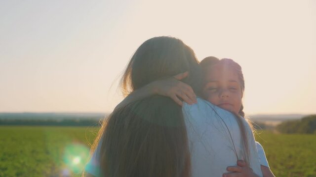 Happy family in the Park. A sweet girl embraces her mother and sister by the neck in the rays of the setting sun. Mom and daughter have fun spending their free time.