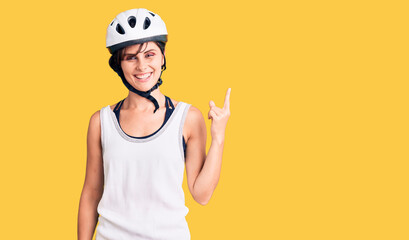 Beautiful young woman with short hair wearing bike helmet smiling happy pointing with hand and finger to the side