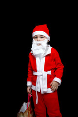 a five-year-old boy in a funny Santa Claus costume stands with a package of gifts. on a black isolated background