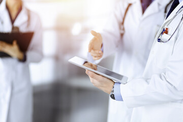Group of unknown doctors use a computer tablet to check up some medical names records, while...