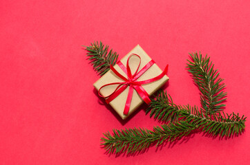 Natural spruce tree branch with a fir cone and Christmas decorations on a red background. Merry christmas and New Year. A minimalist composition, celebration and giving gifts. Copy space, flat lay.
