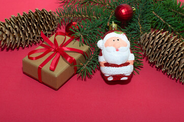 Natural spruce tree branch with a fir cone and Christmas decorations on a red background. Merry christmas and New Year. A minimalist composition, celebration and giving gifts. Copy space, flat lay.