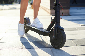 Close-up picture of woman's legs, riding on electric scooter in city center. Female, wearing red...