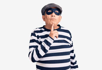 Senior handsome man wearing burglar mask and t-shirt thinking concentrated about doubt with finger on chin and looking up wondering