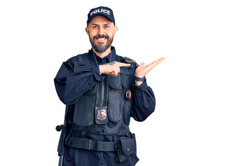 Young handsome man wearing police uniform amazed and smiling to the camera while presenting with hand and pointing with finger.