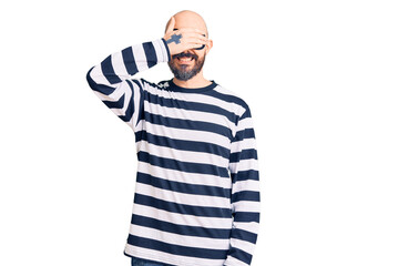 Young handsome man wearing burglar mask smiling and laughing with hand on face covering eyes for surprise. blind concept.