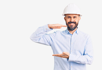 Young handsome man wearing architect hardhat gesturing with hands showing big and large size sign, measure symbol. smiling looking at the camera. measuring concept.