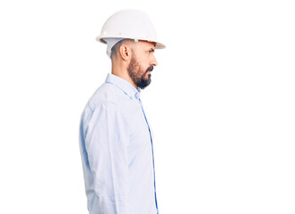 Young handsome man wearing architect hardhat looking to side, relax profile pose with natural face with confident smile.