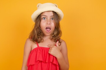 young Caucasian girl standing against yellow background being in stupor shocked, has astonished expression pointing at oneself with finger saying: Who me?
