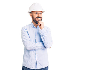 Young handsome man wearing architect hardhat looking confident at the camera with smile with crossed arms and hand raised on chin. thinking positive.