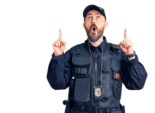 Young handsome man wearing police uniform amazed and surprised looking up and pointing with fingers and raised arms.