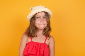 young Caucasian girl standing against yellow background keeps palms together, has pleased...