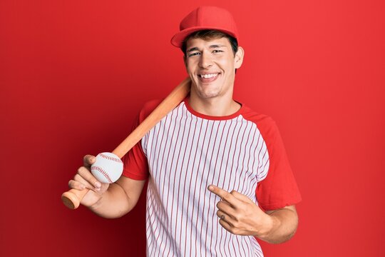 Handsome caucasian man playing baseball holding bat and ball smiling happy pointing with hand and finger