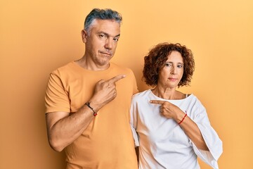 Beautiful middle age couple together wearing casual clothes pointing with hand finger to the side showing advertisement, serious and calm face