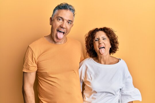 Beautiful middle age couple together wearing casual clothes sticking tongue out happy with funny expression. emotion concept.