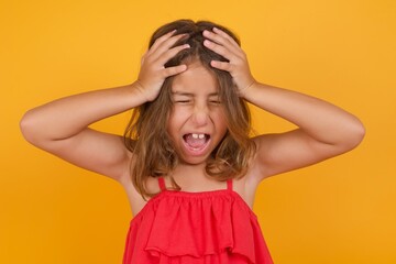 Shocked panic Caucasian young girl standing against yellow background holding hands on head and screaming in despair and frustration.