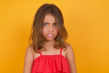 Mad crazy Caucasian young girl standing against yellow background clenches teeth angrily, being annoyed with coming noise. Negative feeling concept.