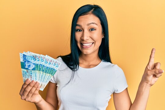 Beautiful hispanic woman holding hong kong 20 dollars banknotes smiling happy pointing with hand and finger to the side