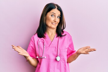 Middle age brunette woman wearing doctor uniform and stethoscope clueless and confused expression...
