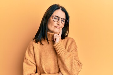 Middle age brunette woman wearing casual winter sweater over yellow background thinking...