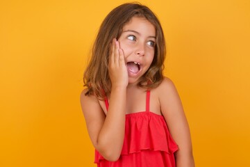 Caucasian young girl standing against yellow background excited looking to the side hand on face. Advertisement and amazement concept.