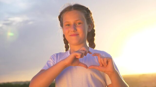 Happy childhood.A cute child at sunset looks into the camera and makes a heart symbol out of his fingers. Heart shape with hands, a sign of love. Concept of health care, vacation, assistance.
