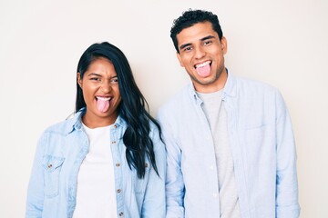 Fototapeta na wymiar Beautiful latin young couple wearing casual clothes sticking tongue out happy with funny expression. emotion concept.